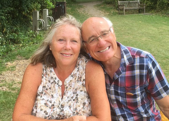 Volunteers, Chris and Margaret sit together in the garden, smiling. Chris leans his head on Margaret.