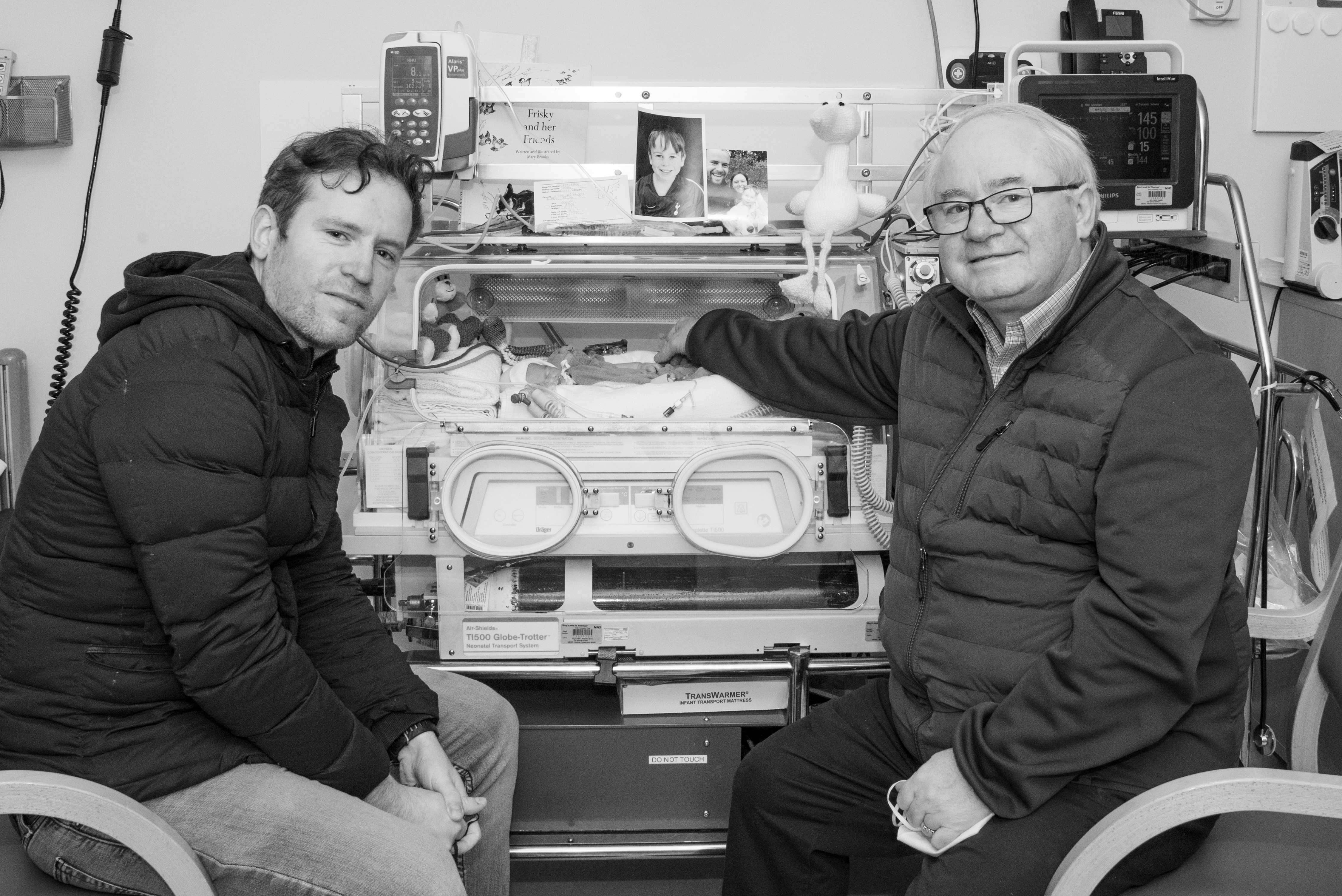 Jade's uncle and grandfather sit next to her as she lays in an incubator.