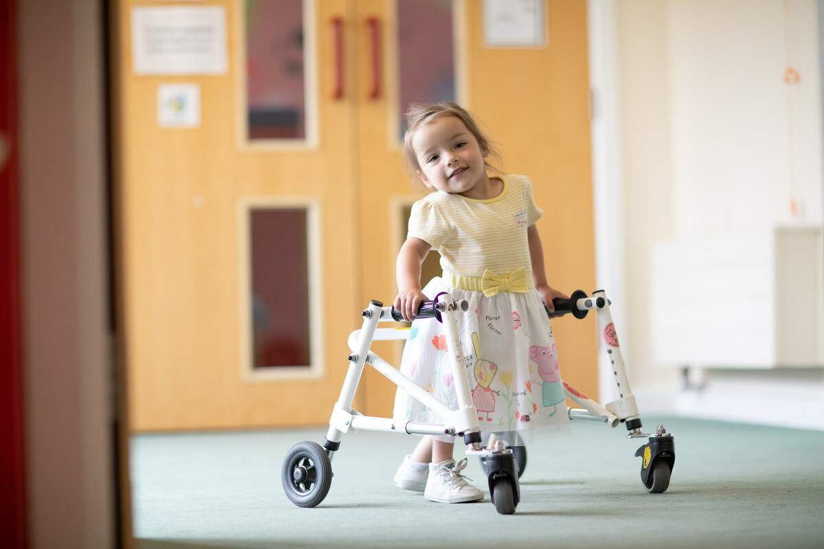 A girl in the corridor, smiling and wearing a Peppa Pig skirt.